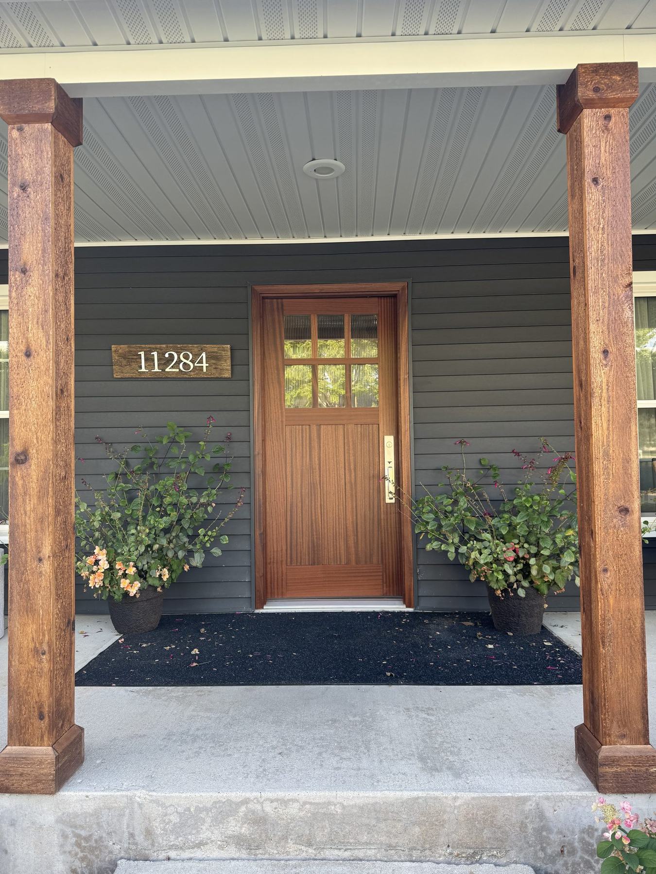 Front porch with charcoal siding, stained wood columns and a stained entry door